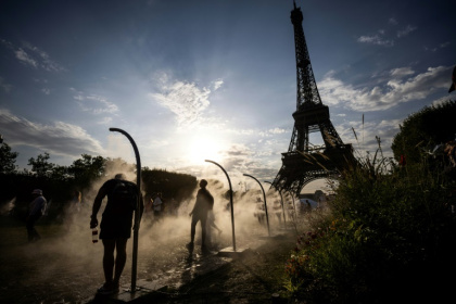 Des passants se rafraîchissent avec des brumisateurs d'eau à côté de la Tour Eiffel à Paris, le 29 juillet 2024 Des passants se rafraîchissent avec des brumisateurs d'eau à côté de la Tour Eiffel à Paris, le 29 juillet 2024
