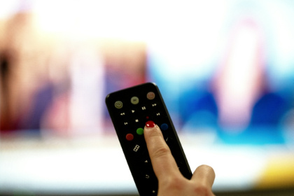 Une personne tient une télécommande pointée vers un écran de télévision, à Paris le 15 janvier 2025 - Anna KURTH (AFP)