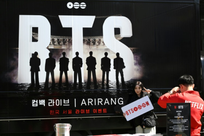 Une femme pose pour une photo devant un camion faisant la promotion du concert de retour du boys band de K-pop BTS à Séoul, le 19 mars 2026 - Jung Yeon-je (AFP)