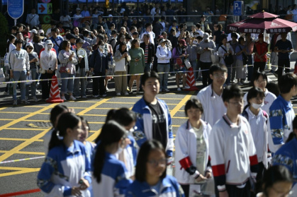 Des lycéens attendent d'entrer dans la salle d'examen pour passer le "gaokao", le concours national d'entrée à l'université, sous les regards de leurs parents maintenus derrière un cordon à l'arrière-plan, le 7 juin 2026 à Pékin - WANG Zhao (AFP)