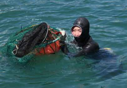 La "femme de la mer" Woo Jung-min nage à l’aide du tewak, une bouée utilisée pour flotter, à Geoje, en Corée du Sud, le 12 août 2026 - Jung Yeon-je (AFP)